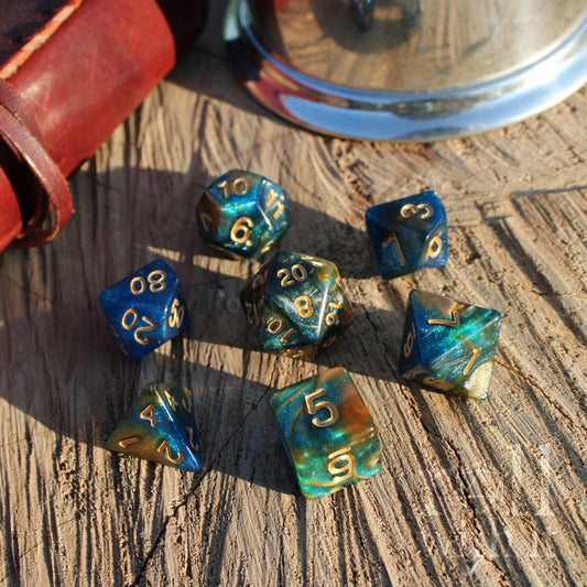 Set of blue and green polyhedral dice on a wooden surface with a leather book in the background.
