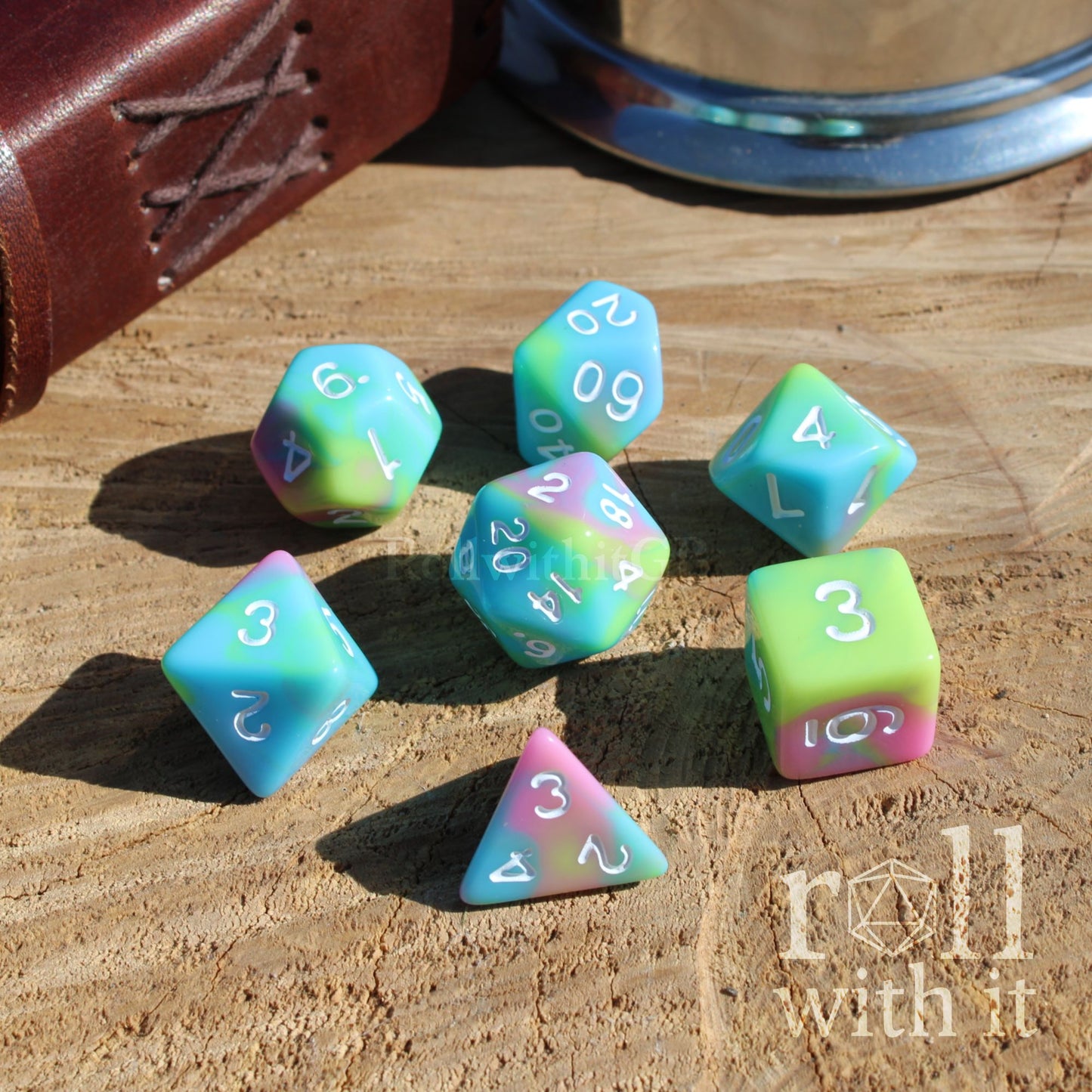 Angle view of 7 pastel rainbow tabletop roleplaying polyhedral dice set on a wooden surface with white ink