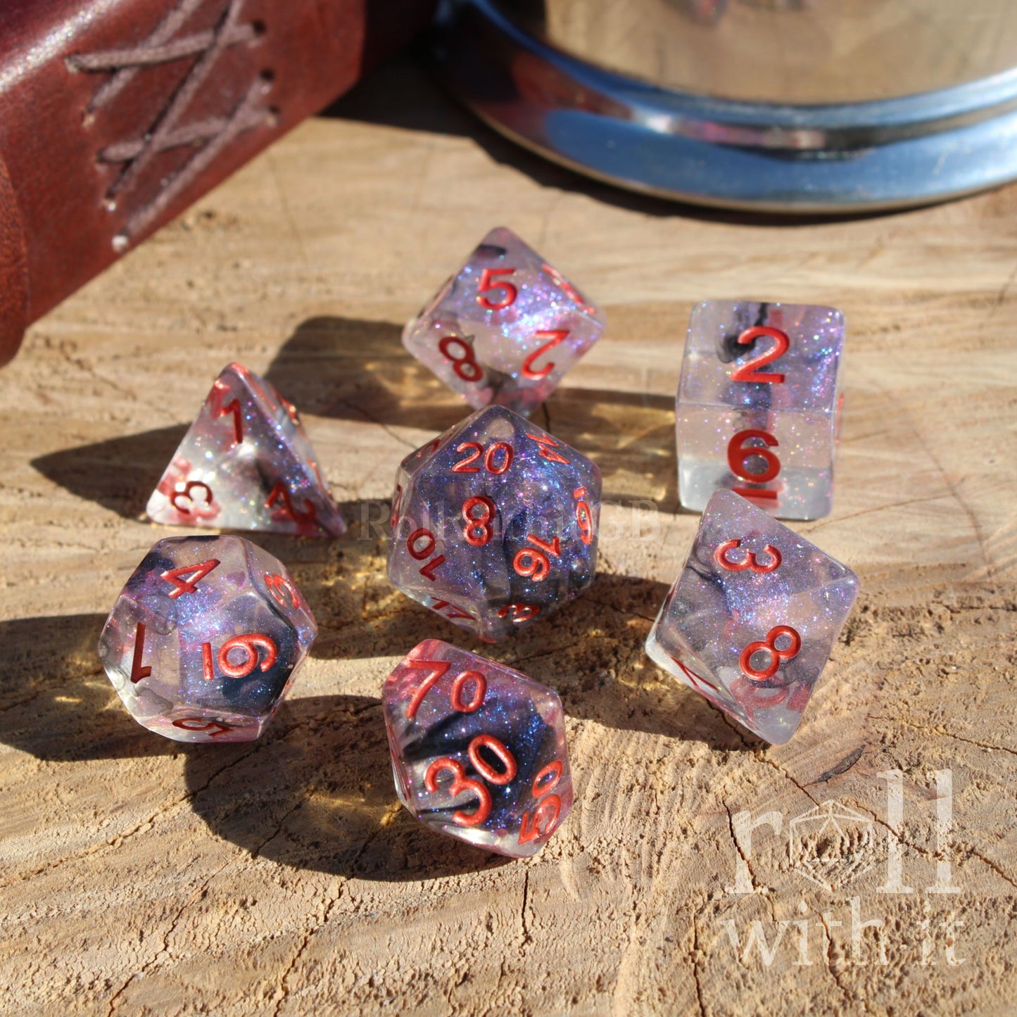 Set of 7 purple and black goth aesthetic polyhedral dice with red numbers on a wooden surface, with 'roll with it' text.