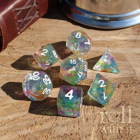 Set of colorful polyhedral dice on a wooden surface with a leather-bound book and metal container in the background.