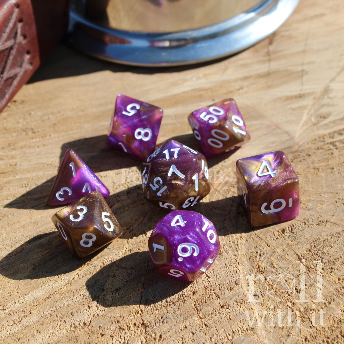 Side view of 7 set of purple and golden galaxy glitter TTRPG polyhedral dice on a wooden surface with white inked numbers