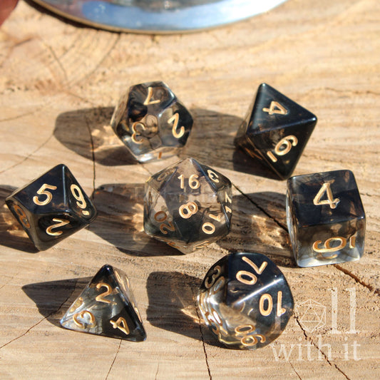 Set of swirling black and clear polyhedral dice with gold numbers on a wooden surface.