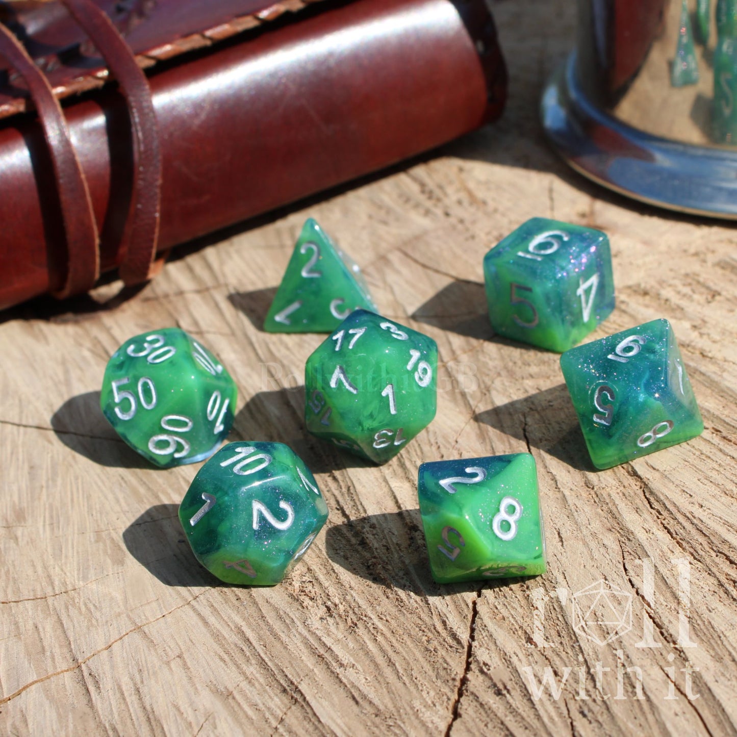 Green blue swirling polyhedral dice set on a wooden surface with a leather-bound book and glass container in the background.