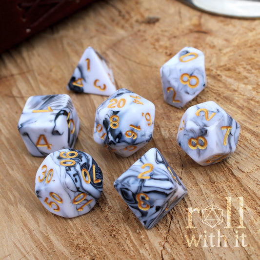 a set of 7 grey black and white shiny polyhedral ttrpg dice on a wooden surface
