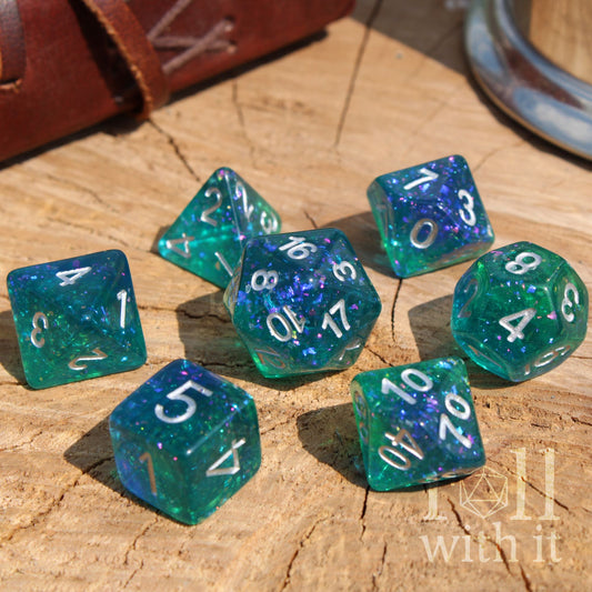 Set of reflective rainbow green and blue dice with numbers on a wooden surface, featuring the brand 'Roll with It'.