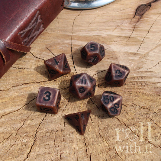 Set of metallic bronze polyhedral dice on a wooden surface with 'roll with it' text.