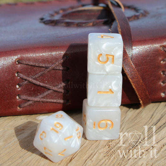 White dice with gold numbers on a wooden surface next to a leather handbook, featuring 'roll with it' branding.