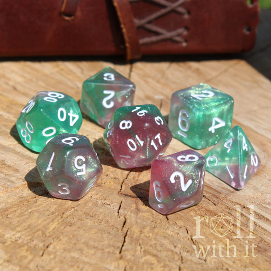 Set of colorful pink pale emerald green resin glow in the dark dnd polyhedral dice on a wooden surface with 'roll with it' text.