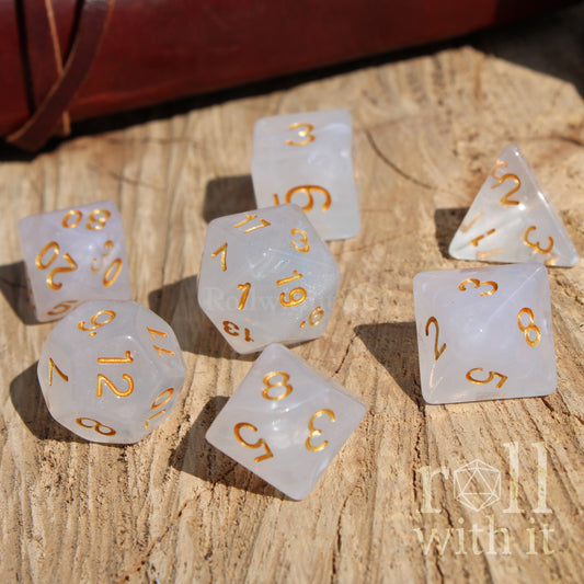 Set of white polyhedral dice with gold numbers on a wooden surface, featuring 'roll with it' branding.