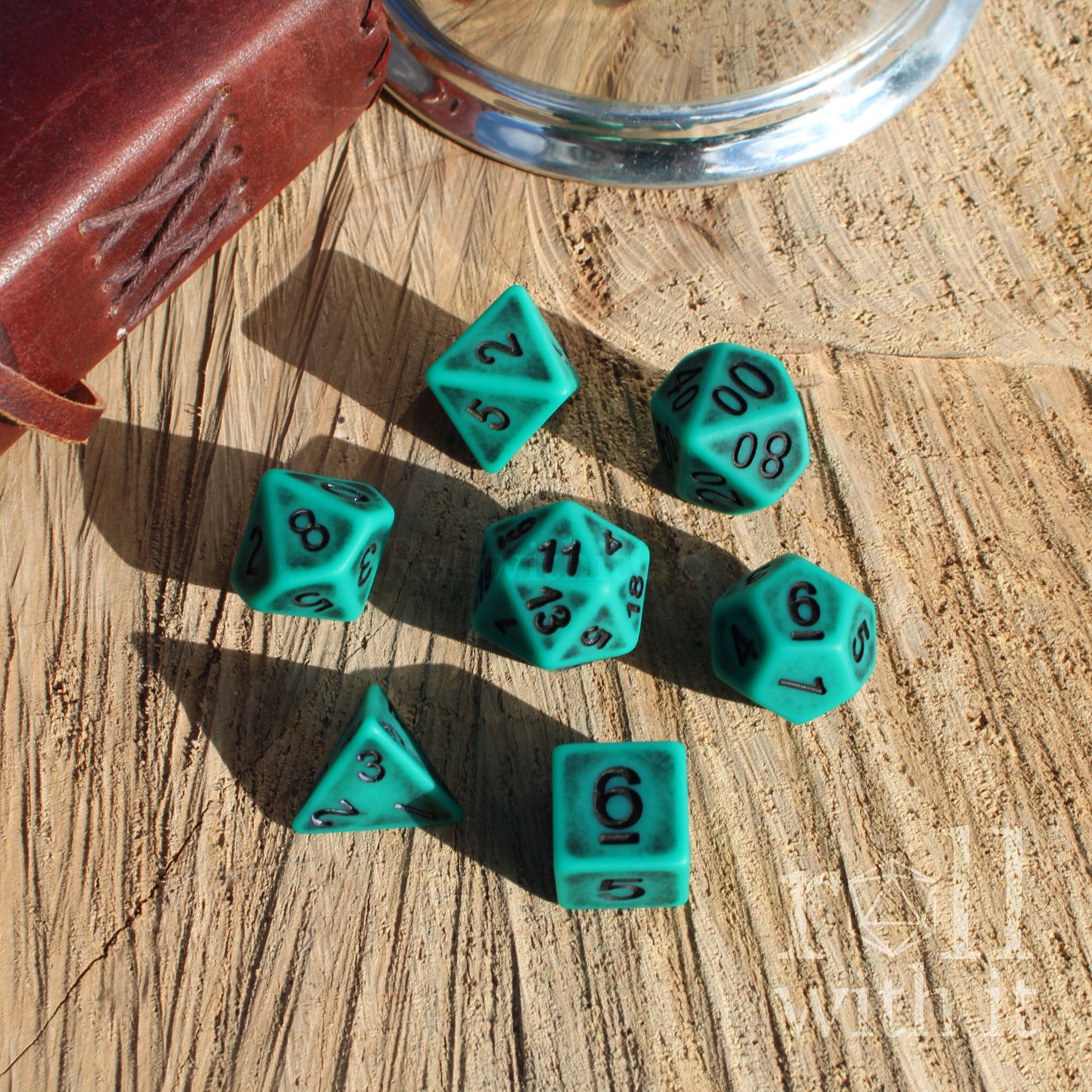 Set of black numbers teal polyhedral dice on a wooden surface with a metal container.
