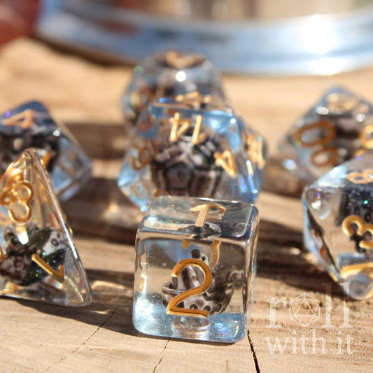 Close side view of 7 pirate ship dice with a miniature ship inside on a blue glitter sea layer