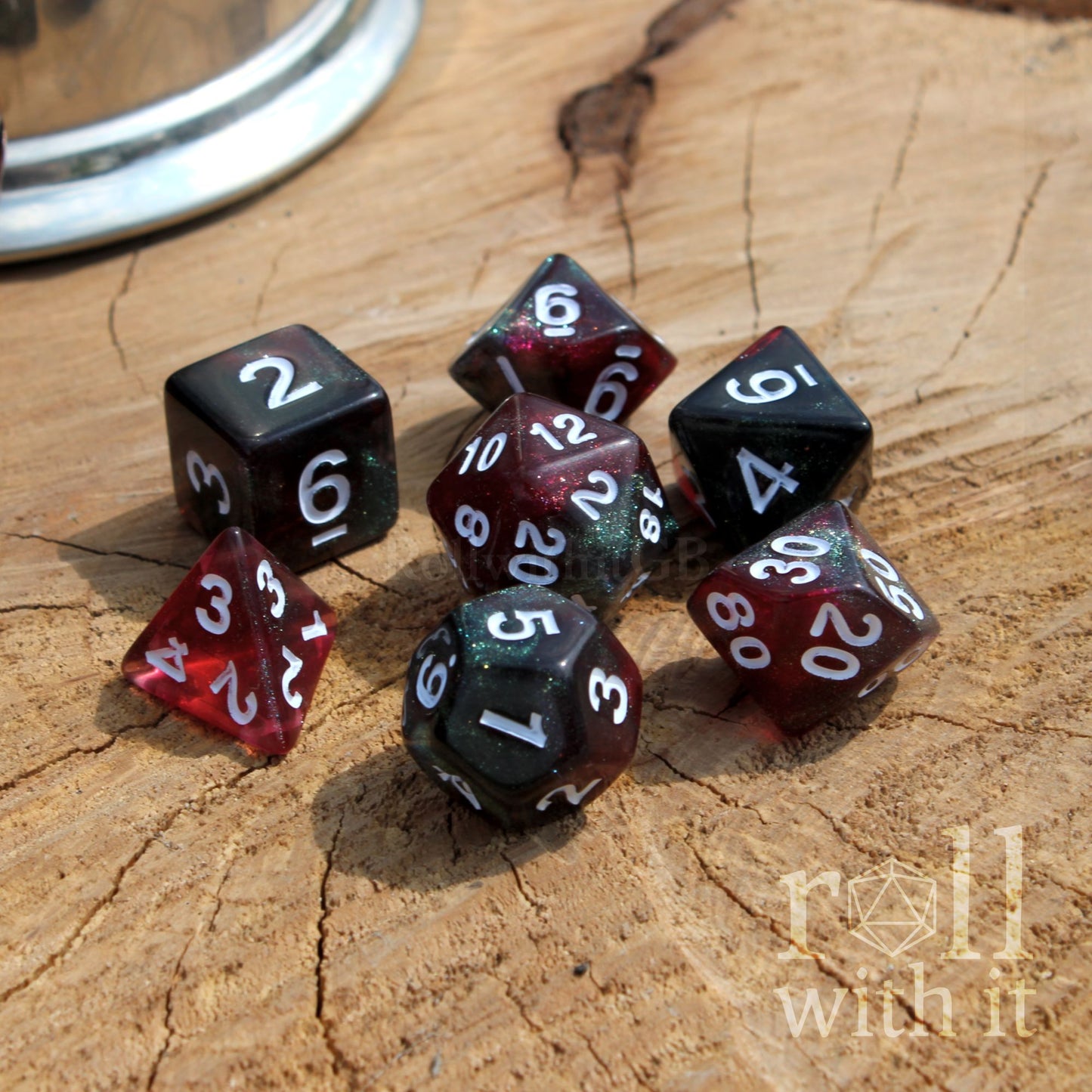 Set of polyhedral dice with red and black faces on a wooden surface, featuring 'roll with it' branding.