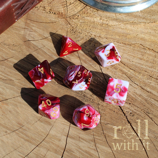 Set of marbled red and pink dice with white streaks on a wooden surface with 'roll with it' text.