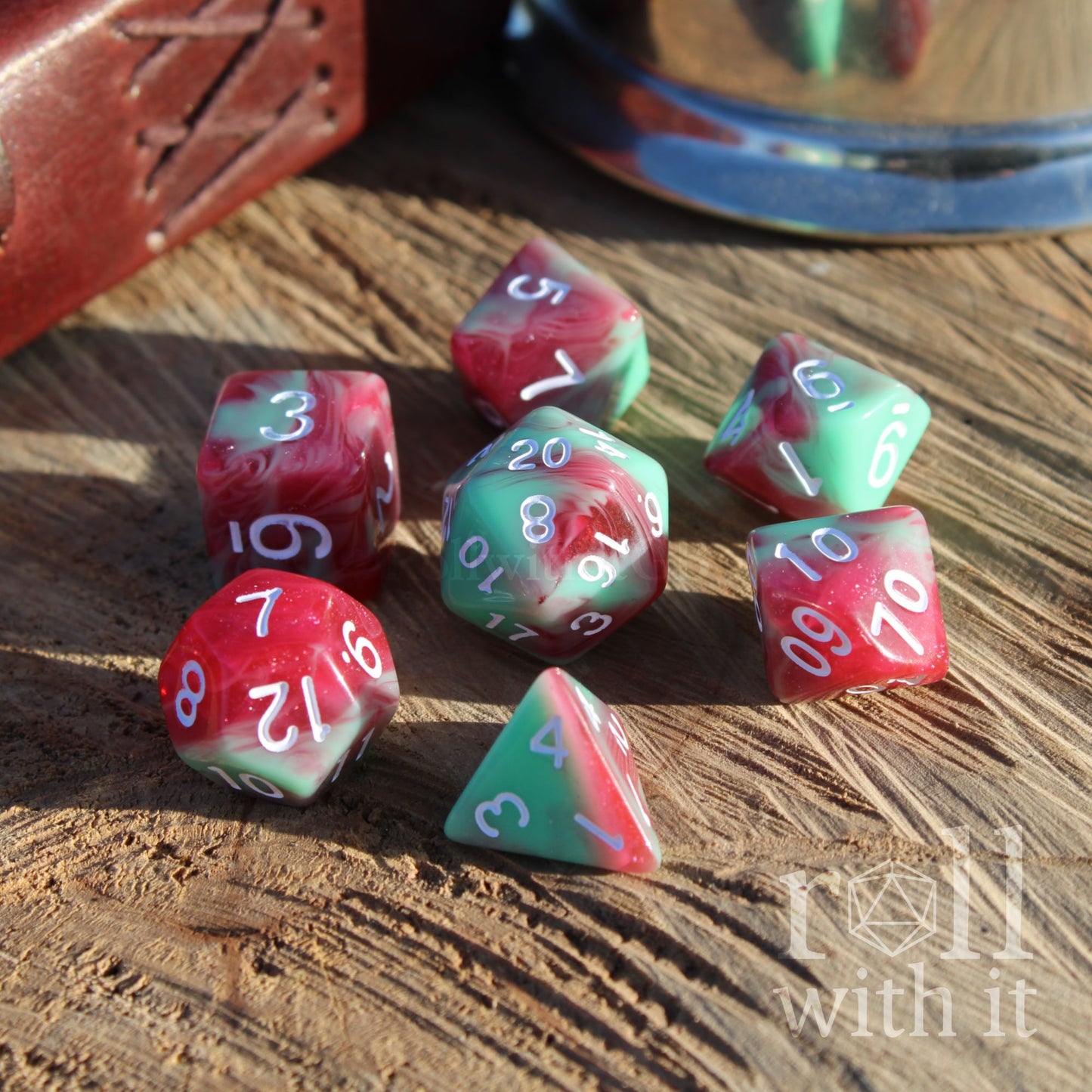 Set of red and green mixed glitter shiny polyhedral dice on a wooden surface with 'Roll with It' branding.