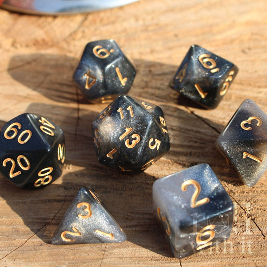 Set of black and white starry glitter filled polyhedral dice with gold numbers on a wooden surface