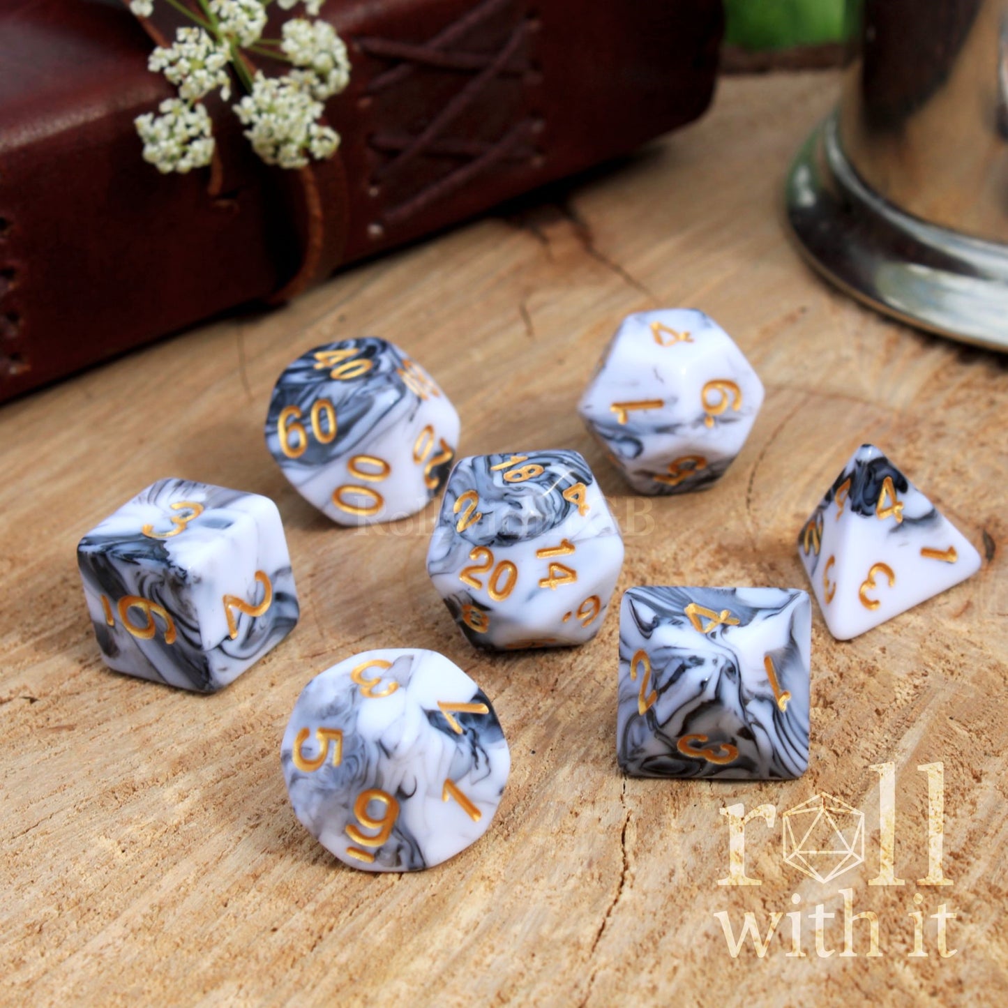 Set of soft simple grey white swirling marbled dice with gold numbers on a wooden surface, featuring the 'roll without it' brand.