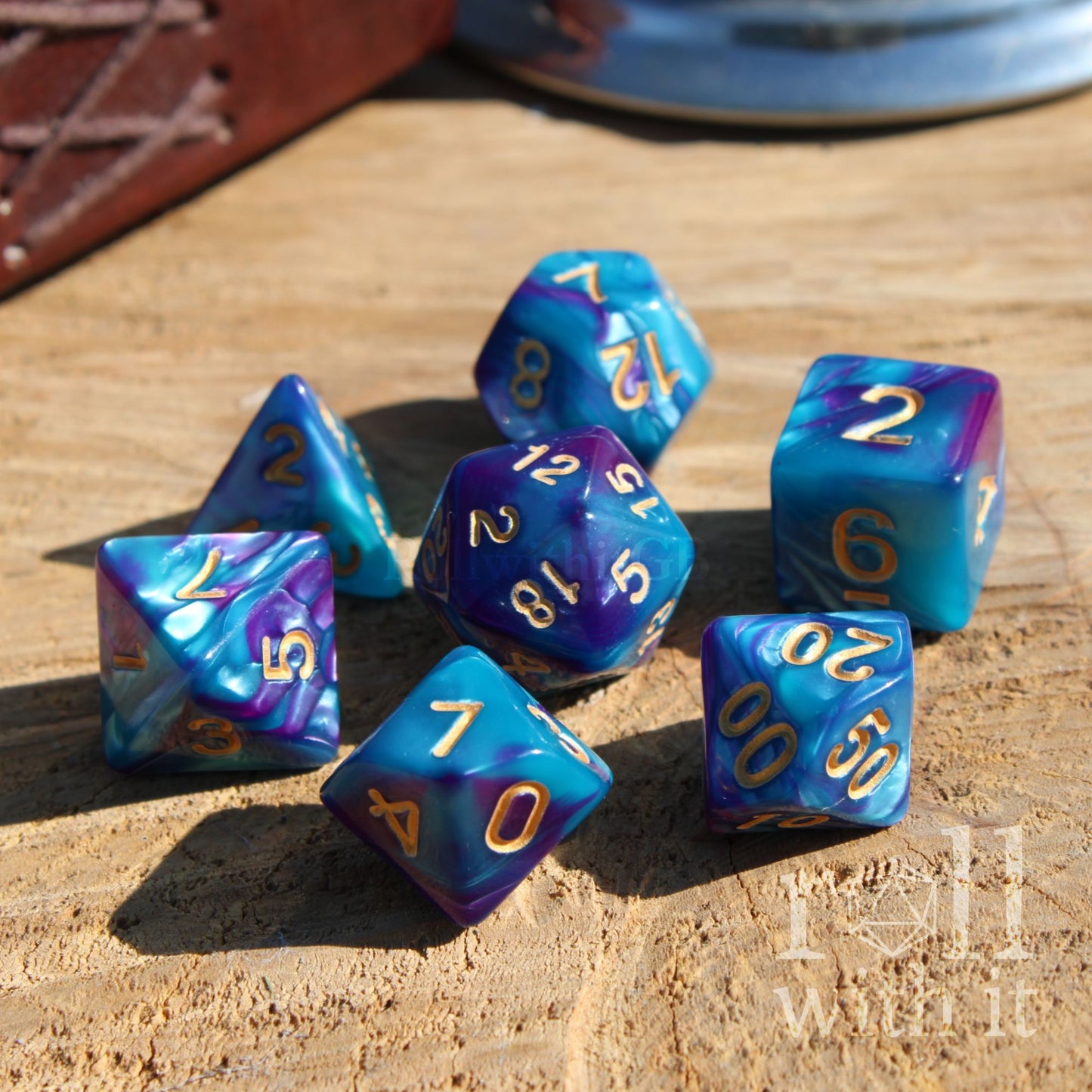 Set of blue and purple polyhedral dice with gold numbers on a wooden surface.