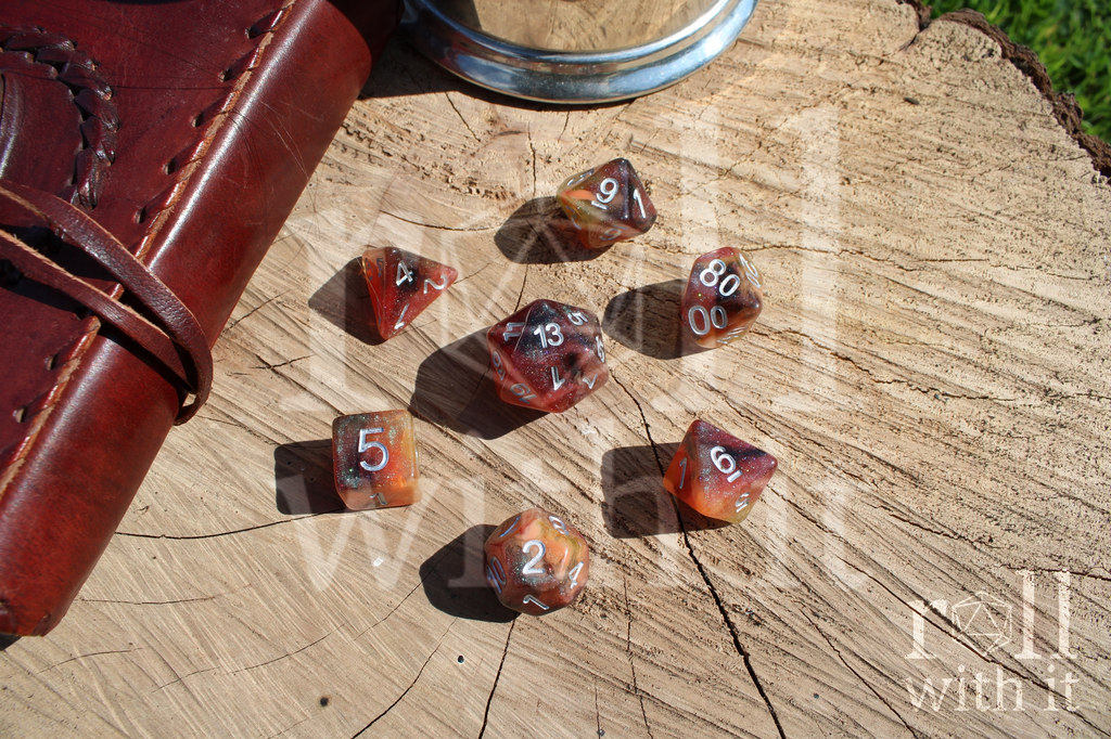 Set of 7 polyhedral roleplaying dice in shades of shimmering orange on an oak base, with tabletop rpg DnD accessories in the background.