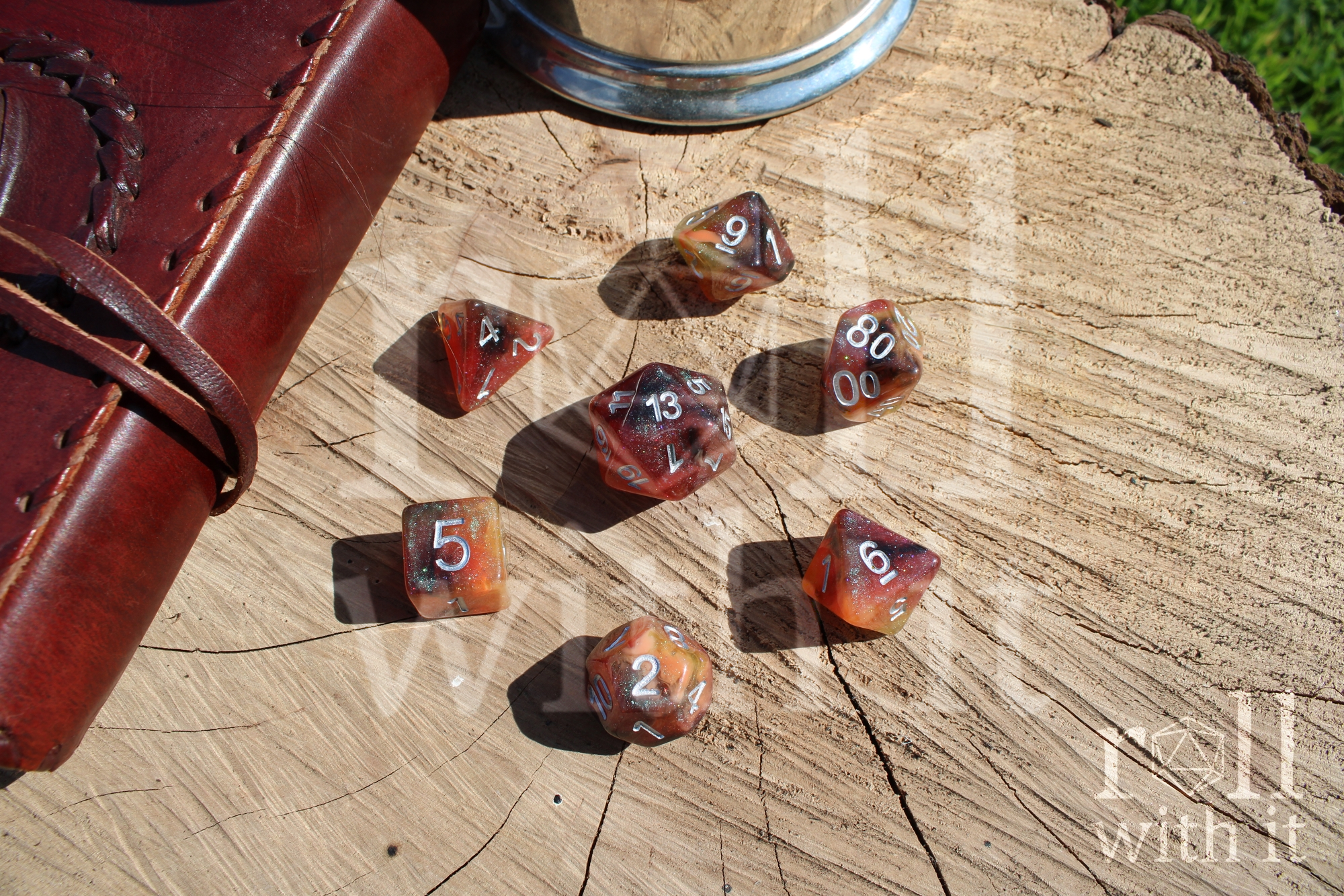 Set of 7 polyhedral roleplaying dice in shades of shimmering orange on an oak base, with tabletop rpg DnD accessories in the background.