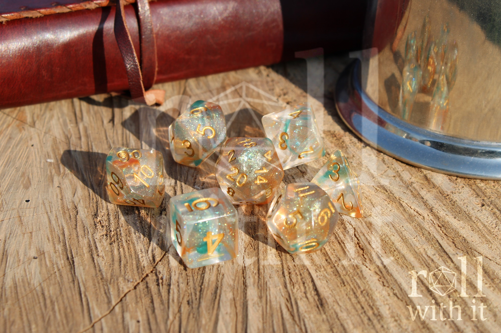 A set of 7 bright glitter filled orange and green tabletop roleplaying dice on a oak base with Dungeons and Dragons accessories in the background