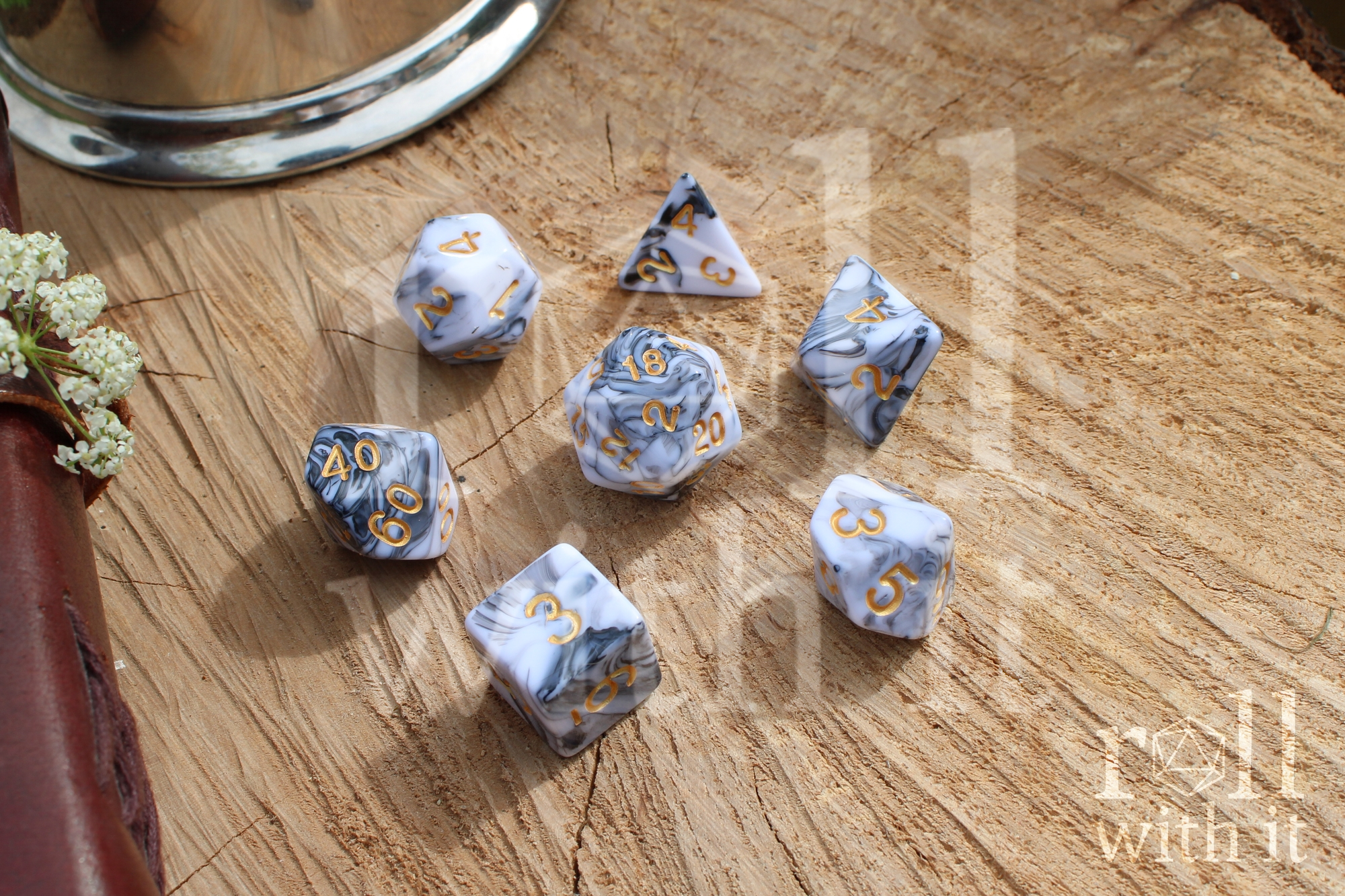 A set of creamy white and grey swirling polyhedral dice on a wooden surface