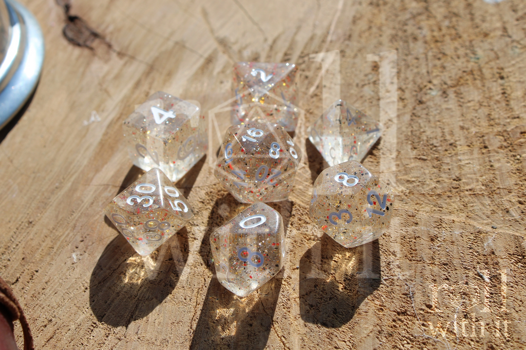 Set of clear polyhedral roleplaying dice with black and orange speckles sat on a wooden log