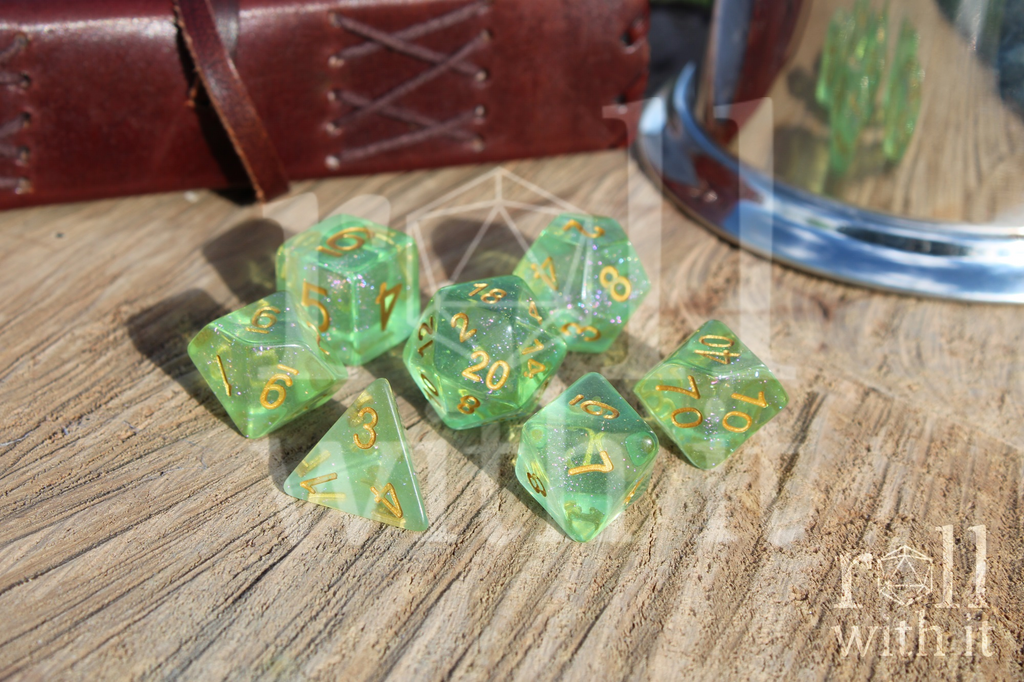 Set of shimmering green polyhedral role playing dice with gold numbers on a wooden surface.