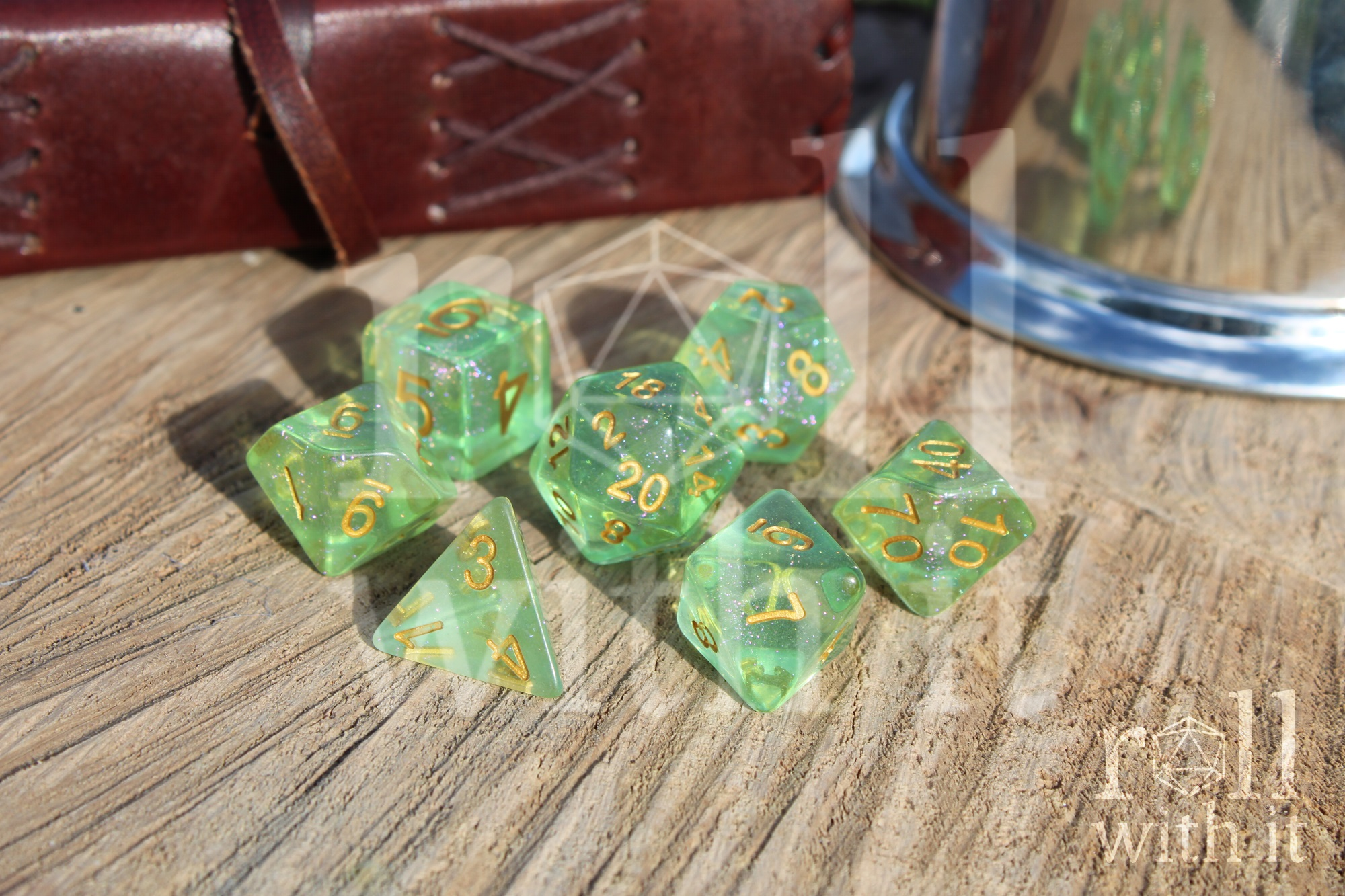 Set of shimmering green polyhedral role playing dice with gold numbers on a wooden surface.