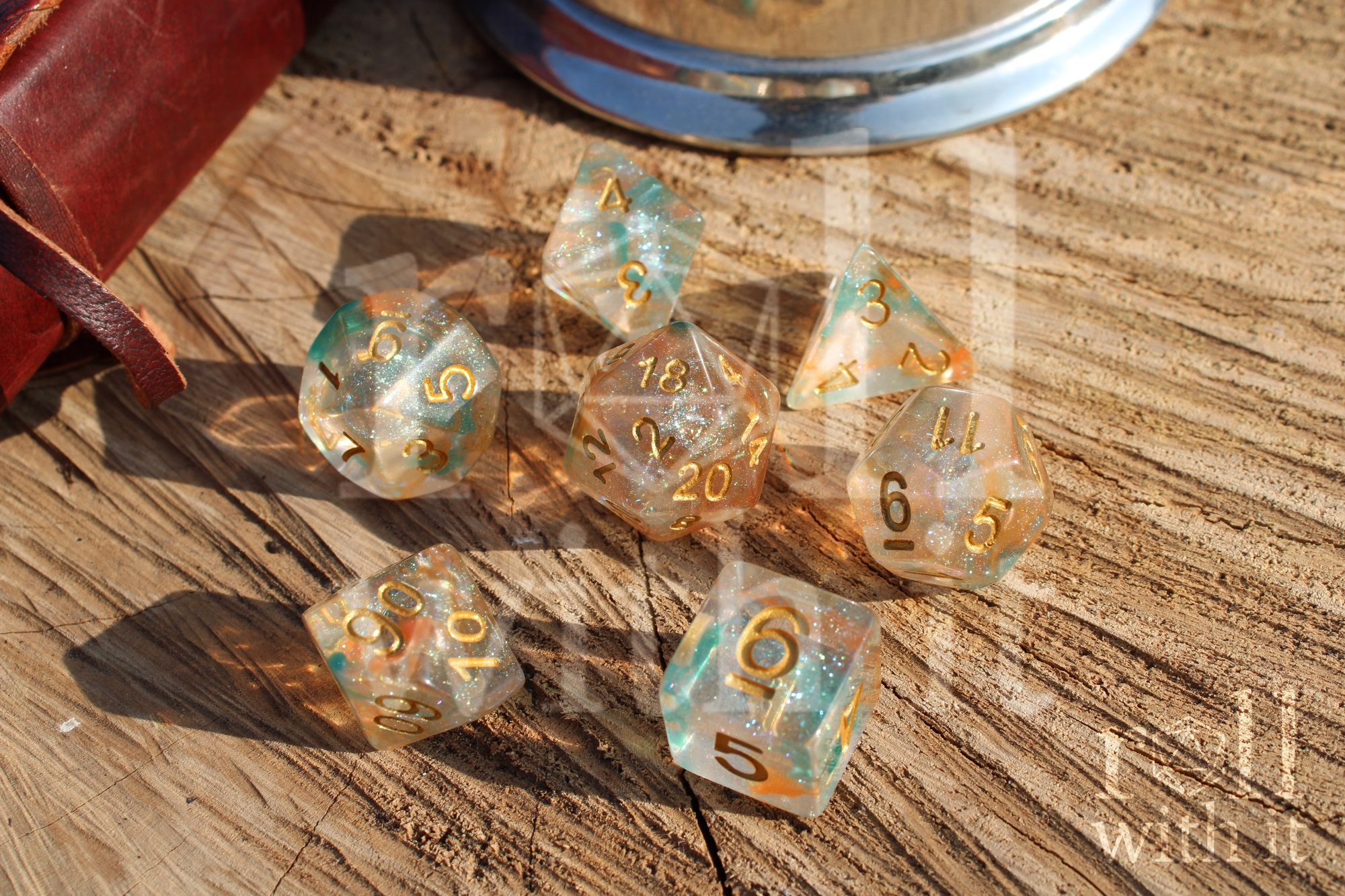 A set of 7 bright glitter filled orange and green tabletop roleplaying dice on a oak base with Dungeons and Dragons accessories in the background