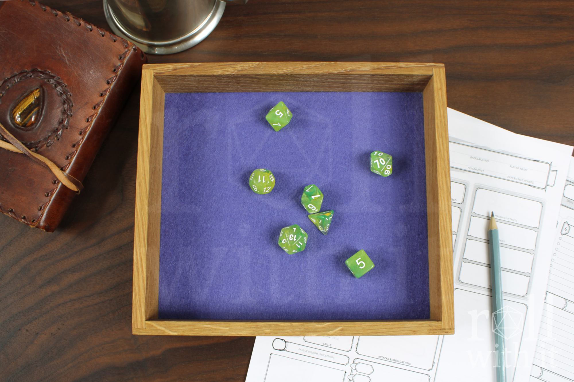 Green polyhedral roleplaying dice on a violet purple felt base inside a wooden oak dice throwing tabletop tray, on a walnut table with a leather case and character sheet in the background.