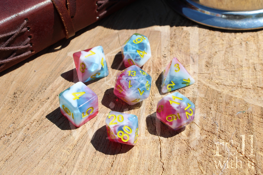 Set of tabletop roleplaying polyhedral dice with pink, white and blue swirls on a wooden base