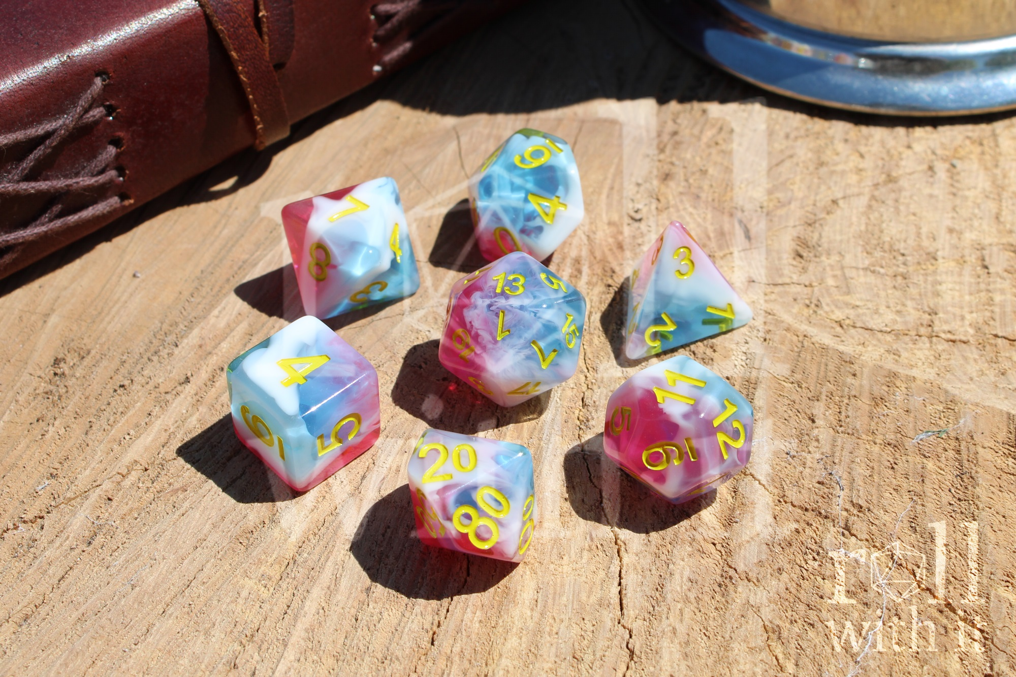 Set of tabletop roleplaying polyhedral dice with pink, white and blue swirls on a wooden base