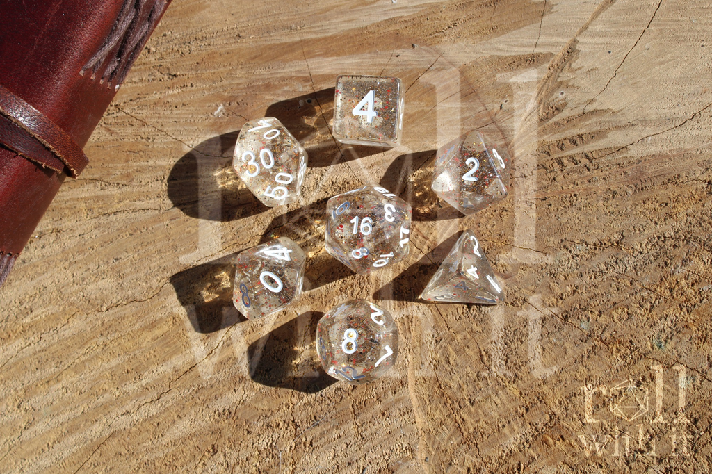 Clear polyhedral role playing dice set with range and black speckles, sat on a wooden log base