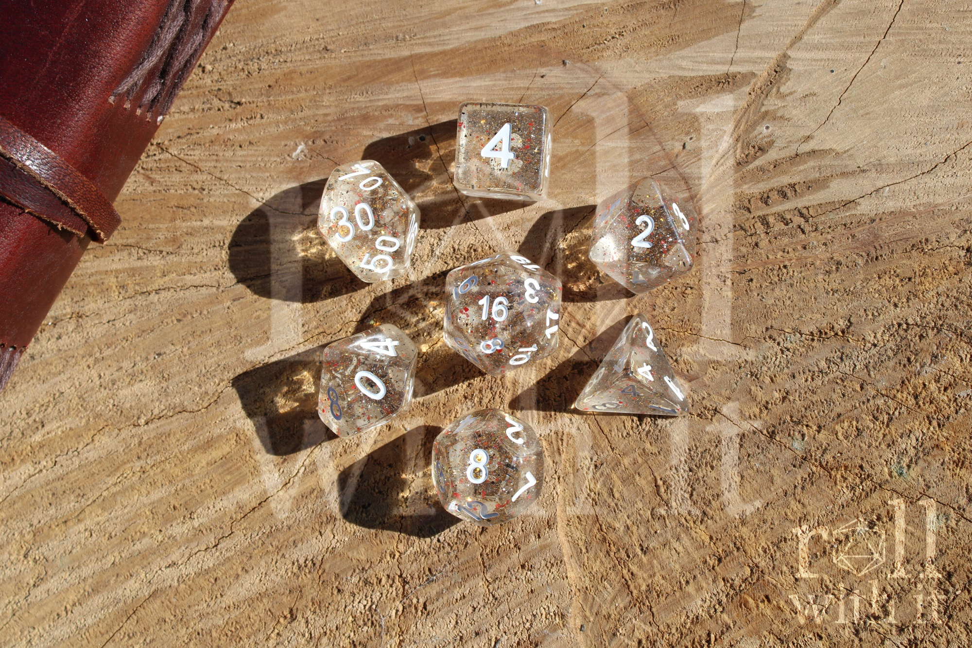 Clear polyhedral role playing dice set with range and black speckles, sat on a wooden log base