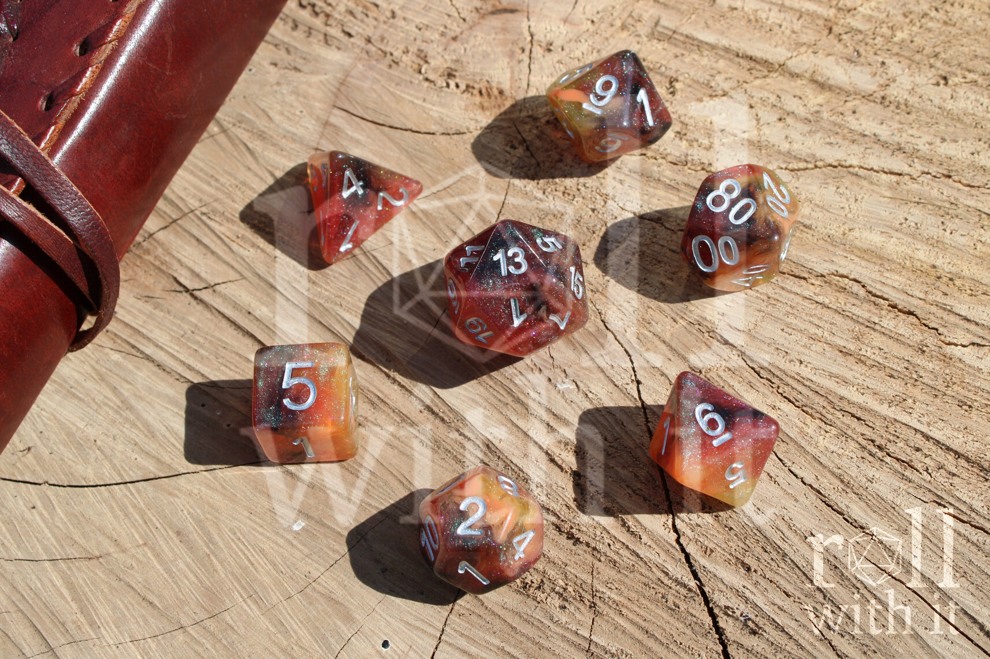 Set of glittery burnt orange polyhedral roleplaying dice on a wooden oak surface with a leather journal in the corner.
