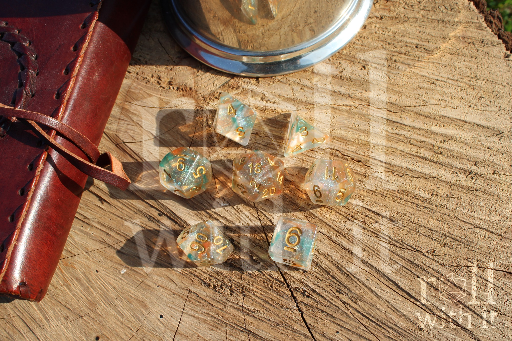 A set of 7 bright glitter filled orange and green tabletop roleplaying dice on a oak base with Dungeons and Dragons accessories in the background