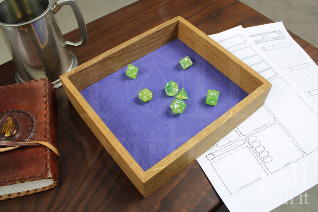 Green Dungeons and Dragons RPG dice sat on a purple violet felt base in a wooden white oak tabletop dice tray on a table, surrounded by character sheets, a pewter tankard and a leather bound journal.