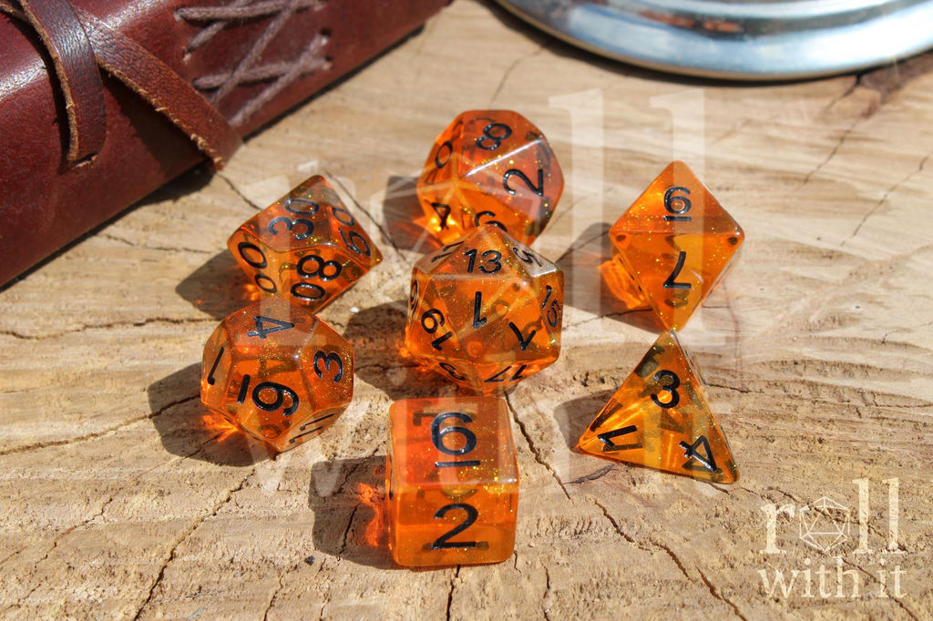 Set of glittery orange polyhedral roleplaying dice with black numbers sat on a wooden surface.