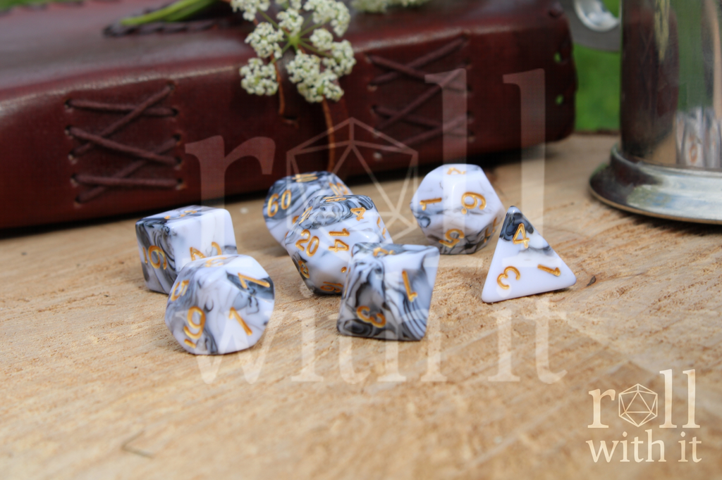 A set of creamy white and grey swirling polyhedral dice on a wooden surface