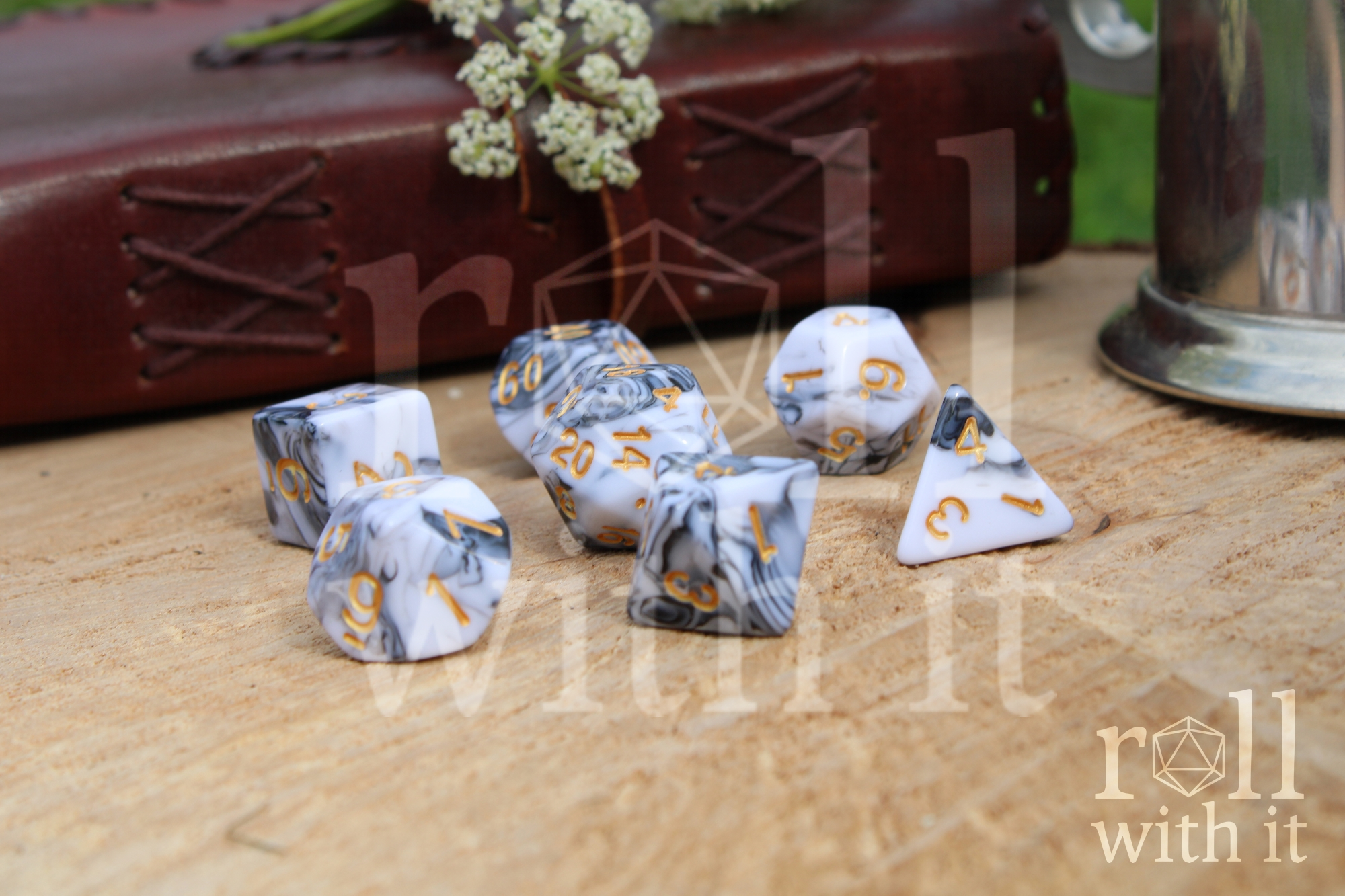 A set of creamy white and grey swirling polyhedral dice on a wooden surface