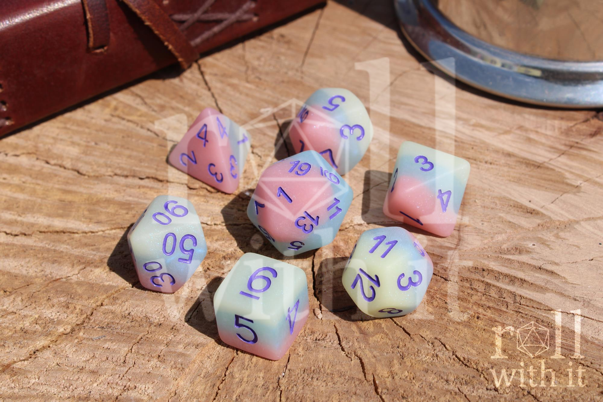 Set of matt pastel-coloured polyhedral dice with numbers on a wooden surface, featuring 'roll with it' branding.