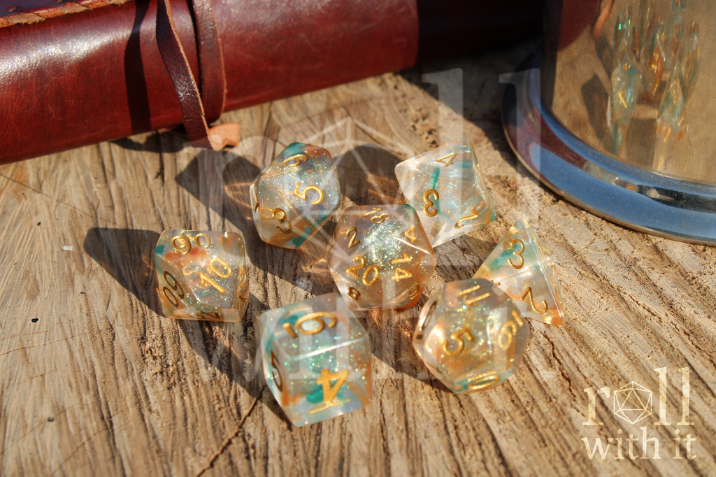 A set of 7 bright glitter filled orange and green polyhedral tabletop roleplaying dice on a oak base with Dungeons and Dragons accessories in the background