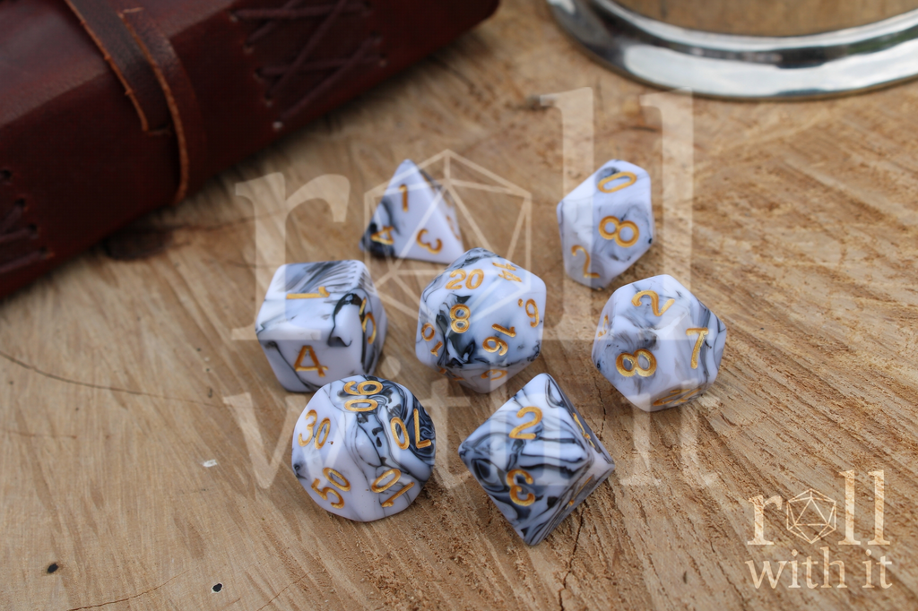 A set of creamy white and grey swirling polyhedral dice on a wooden surface