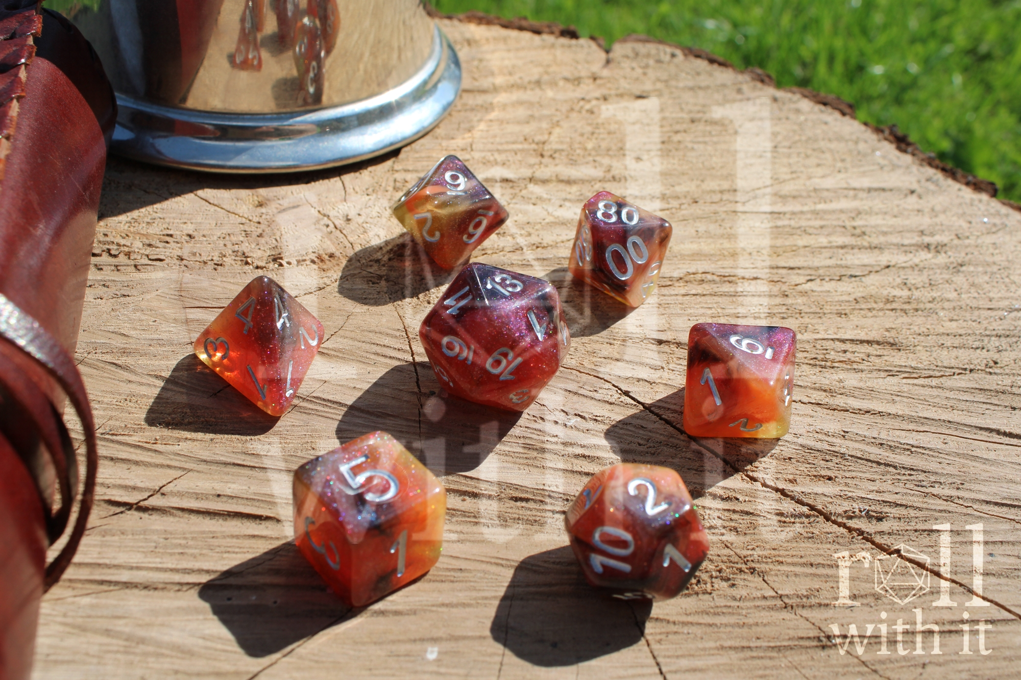 Shimmering orange polyhedral role-playing dice on a wooden base with Dungeon and Dragons accessories are in the background.