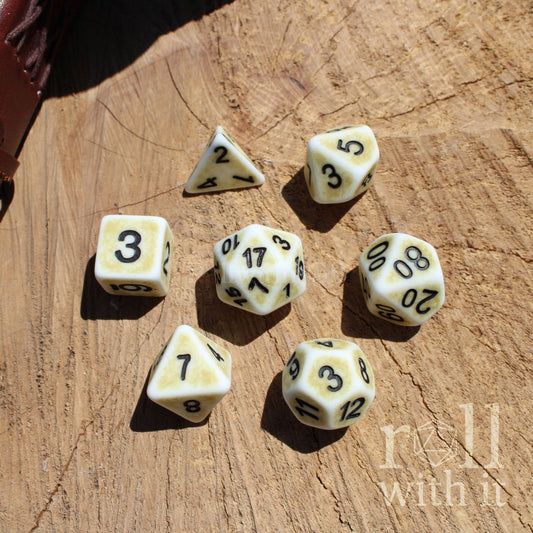Set of 7 worn matte bone white aesthetic D&D roleplaying dice set on a wooden surface