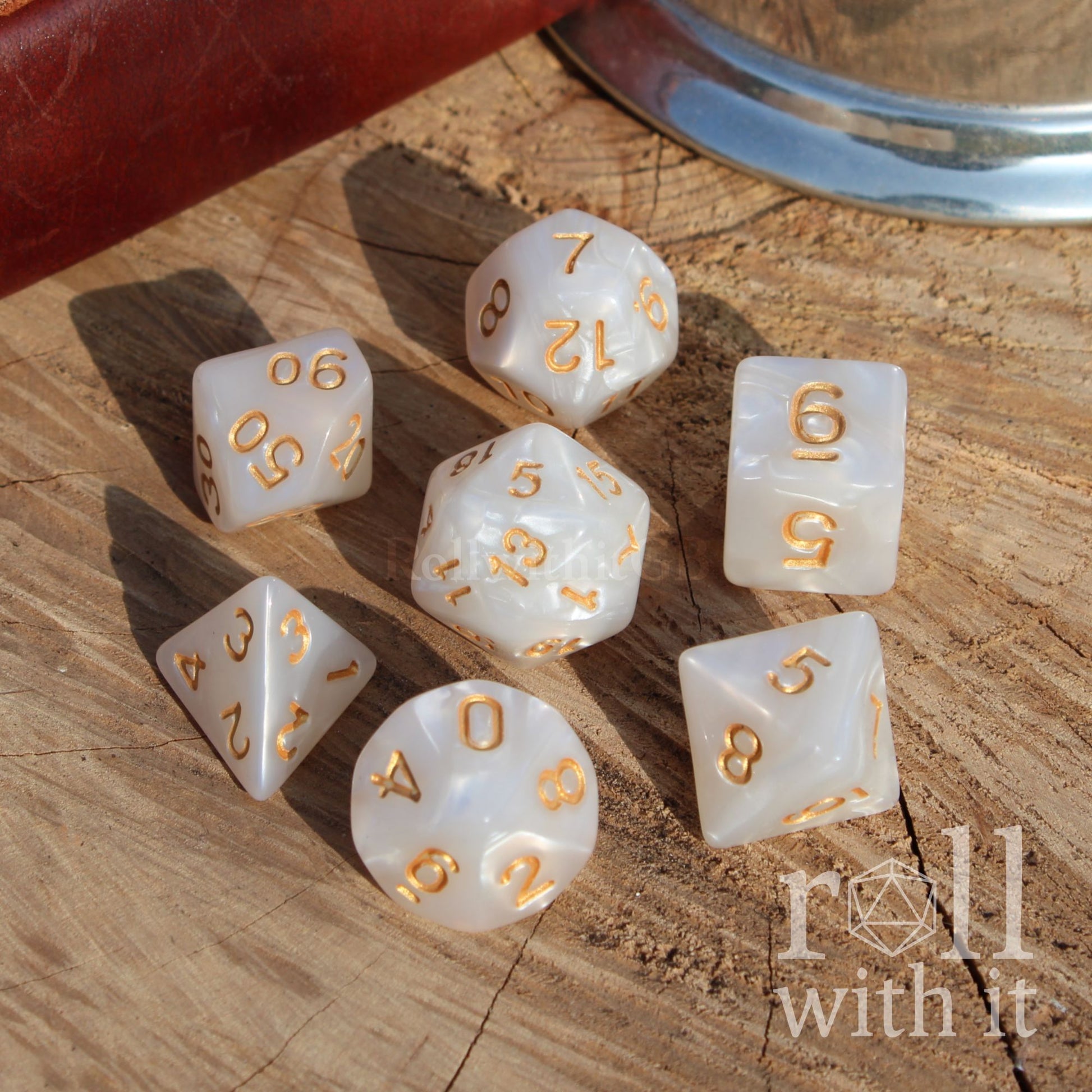 Set of white dice with gold numbers on a wooden surface, featuring the 'roll with it' brand.