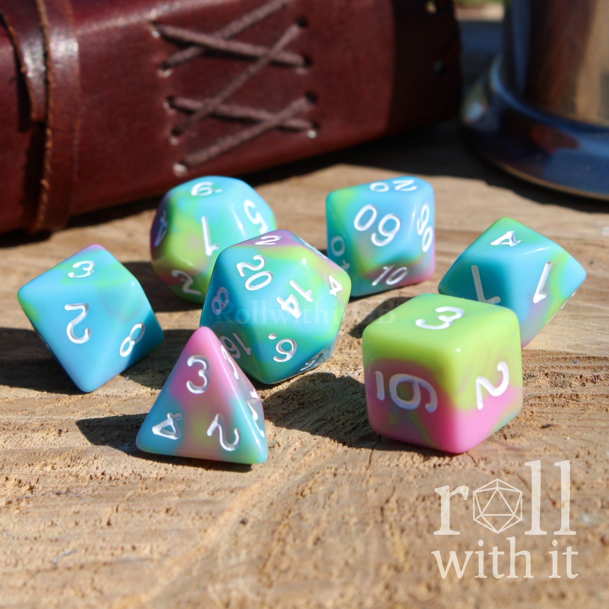 Side view of 7 cute pastel fantasy clowncore D&D compatible polyhedral dice with white easy to read numbers on a wooden surface