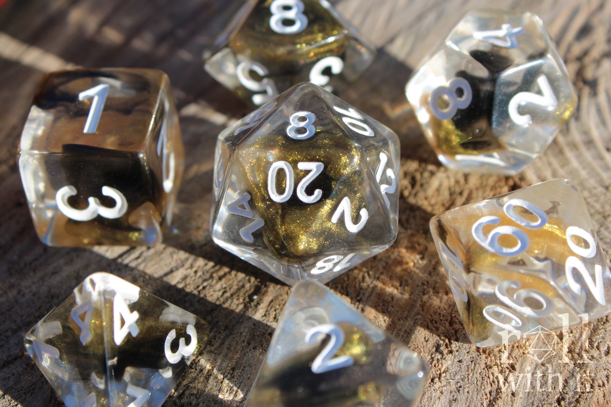 Set of clear polyhedral DND dice with gold and black glittering centres, with white numbers on a wooden surface