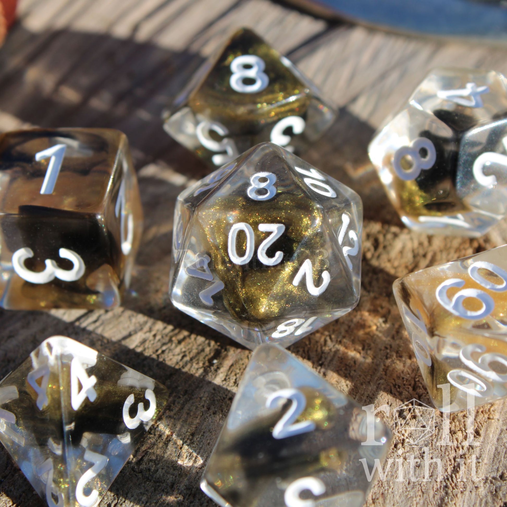 Set of clear polyhedral DND dice with gold and black glittering centres, with white numbers on a wooden surface
