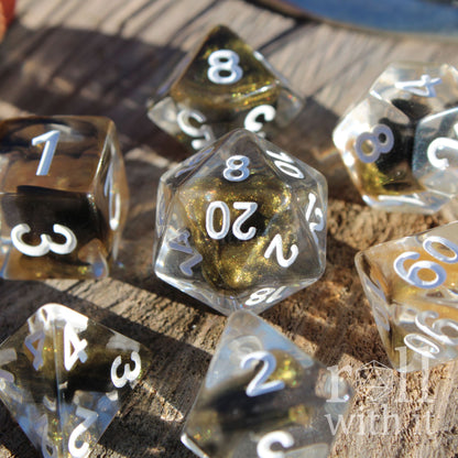 Set of clear polyhedral DND dice with gold and black glittering centres, with white numbers on a wooden surface